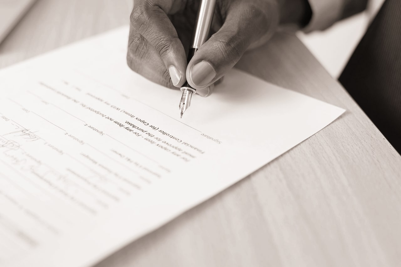 Mão assinando um documento sobre a mesa